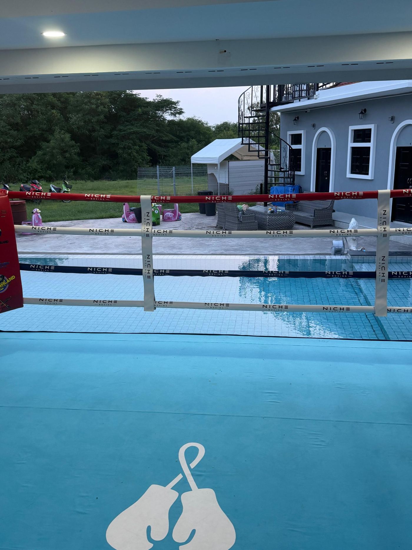 The Niche Boxing ring with its gloves logo on the canvas, the pool and guest rooms behind